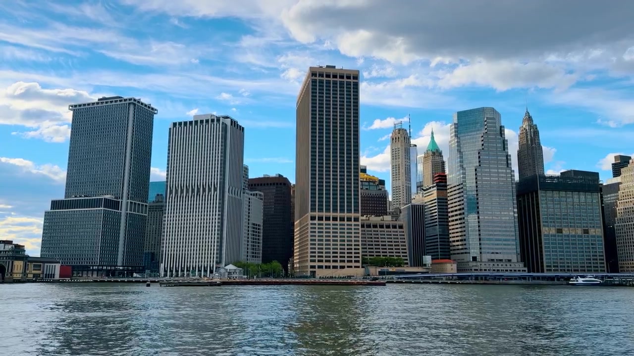 Vista panorâmica do horizonte do Distrito Financeiro de Lower Manhattan a partir das águas do East River, destacando arranha-céus modernos e edifícios icônicos.