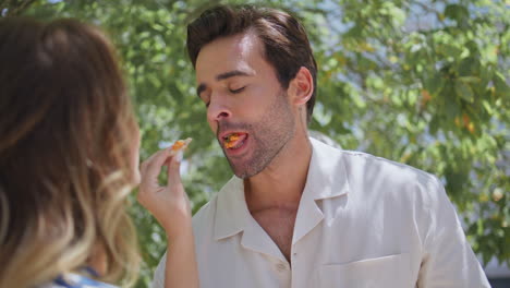 woman feeding handsome boyfriend at summer garden closeup. lovers romantic date