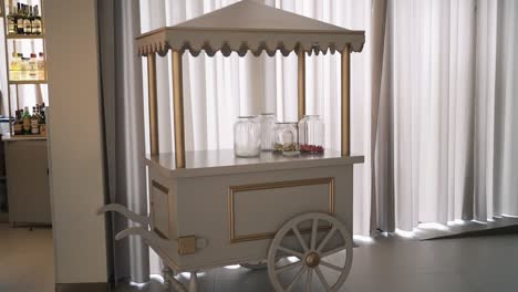 Elegant-wooden-cart-with-glass-jars,-set-against-white-curtains-in-a-modern-interior