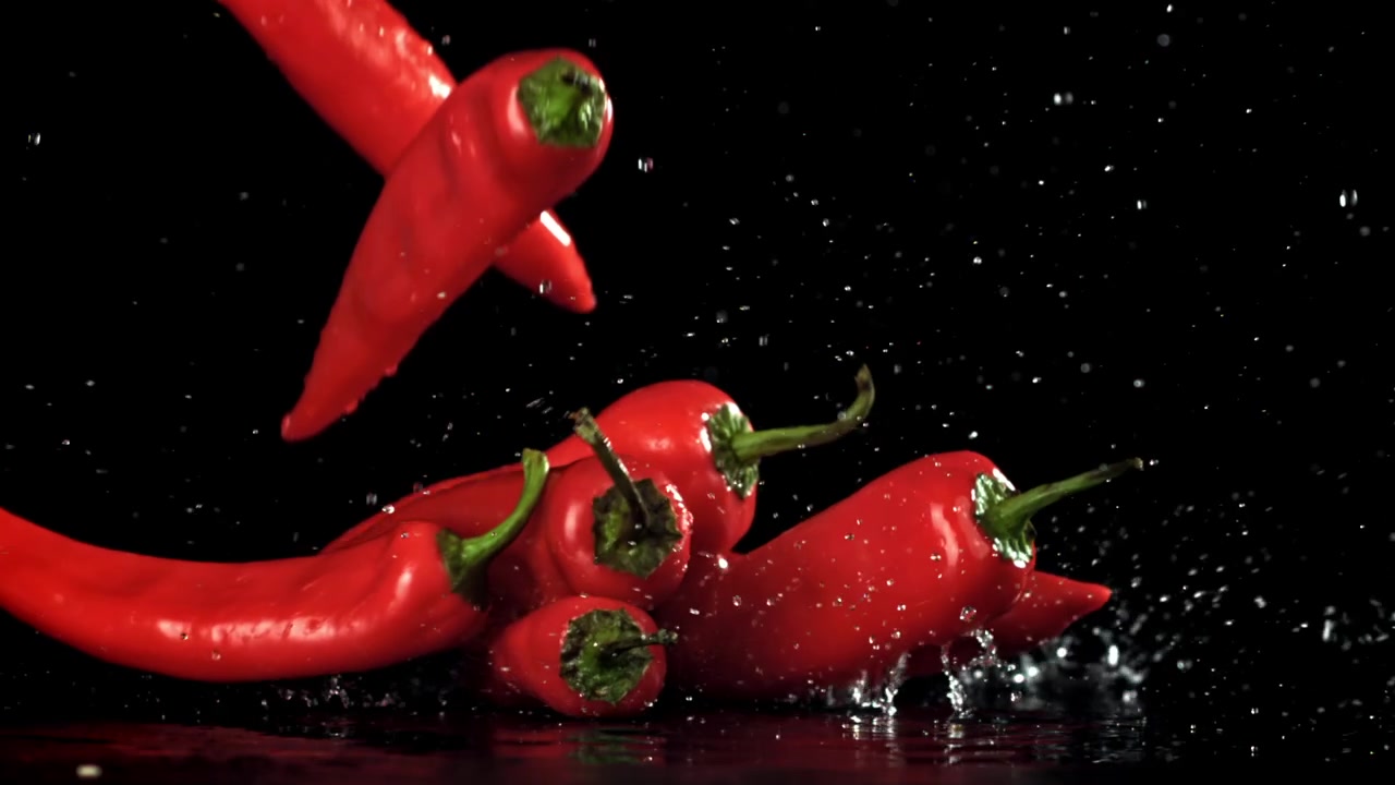 Red Chili Peppers Falling into Water with Splashes in Slow Motion