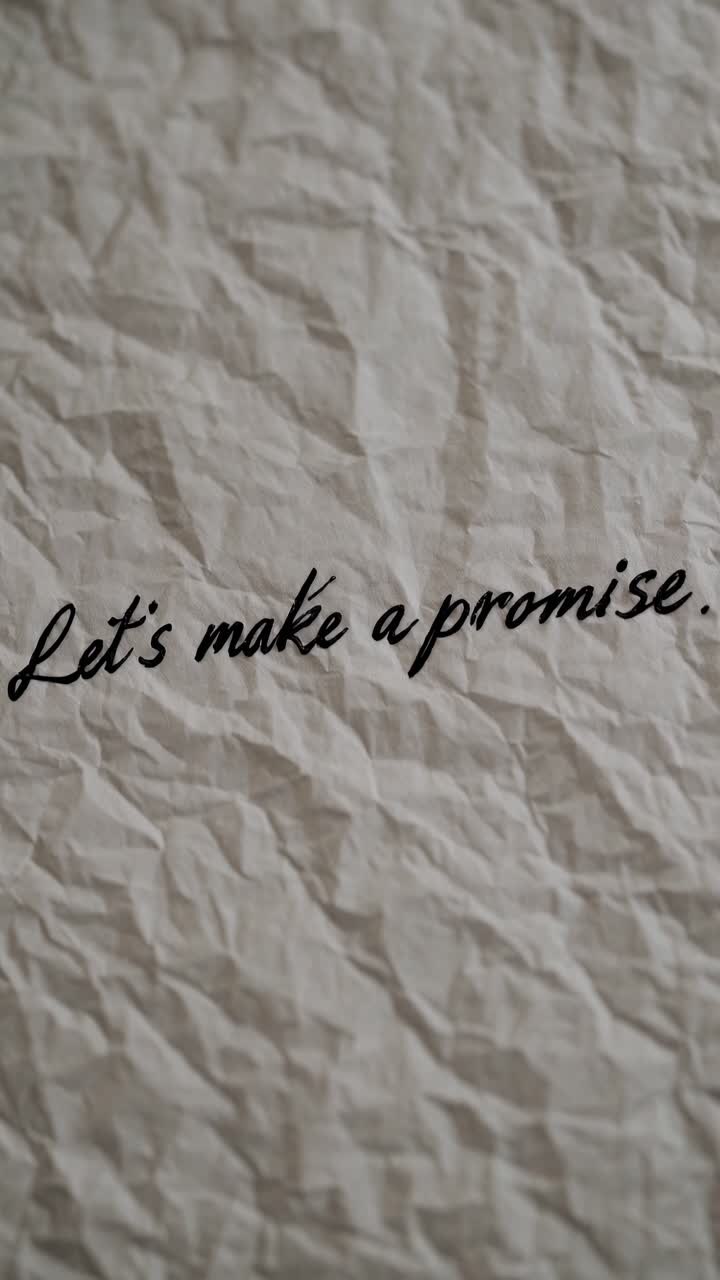 Close-up video shot of crumpled paper with handwritten text 'Let's make a promise,'