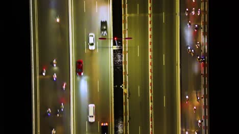 Top-down drone shot of heavy traffic on a central bridge over the Saigon River in Ho Chi Minh City, Vietnam, illuminated by city lights and billboard signs.