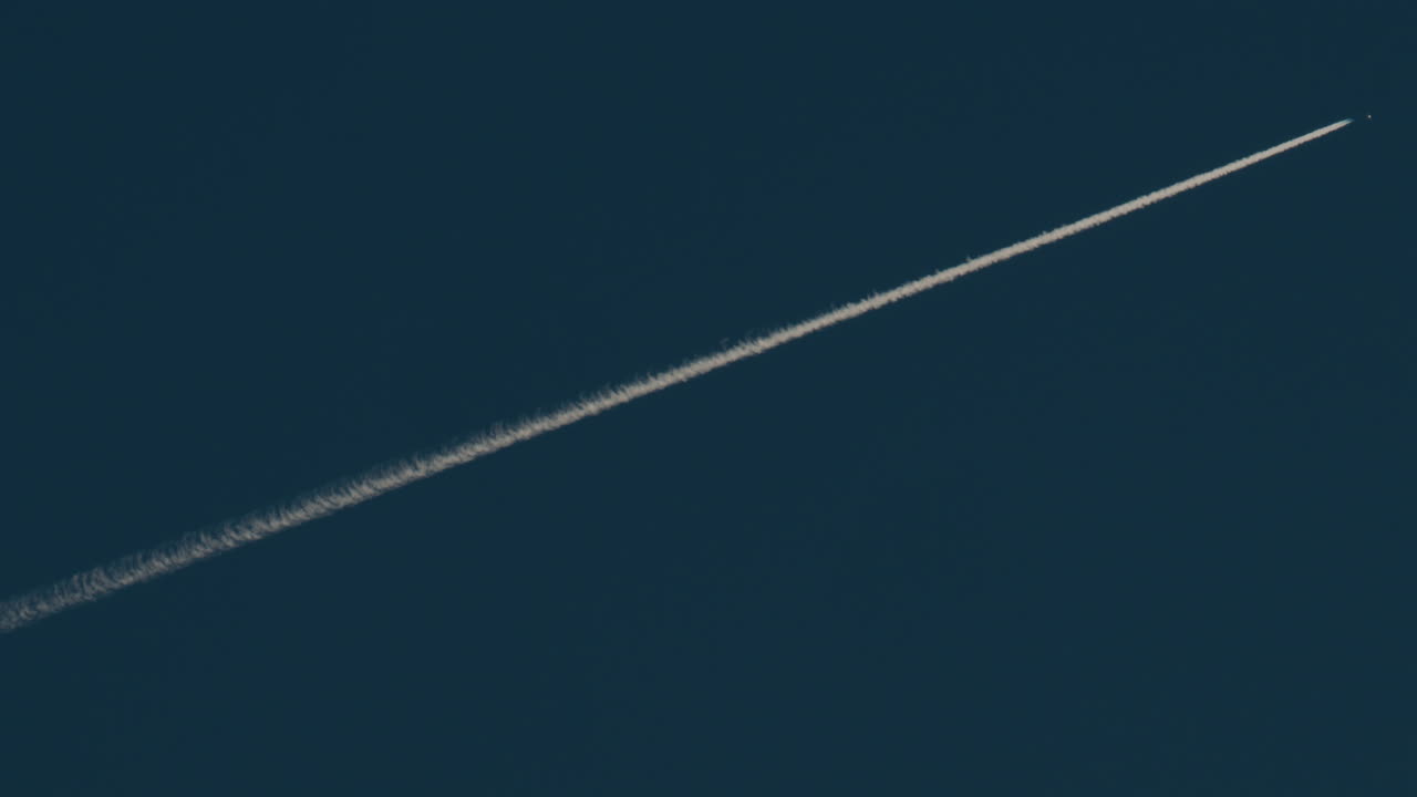 Airplane flying high above leaving long contrails in a clear blue sky