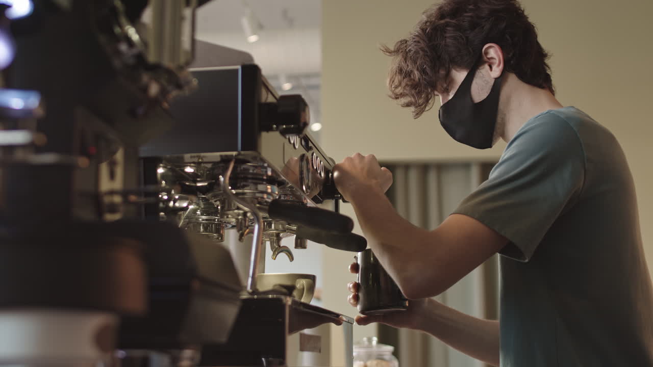 Giovane barista che prepara un cappuccino usando la macchina del caffè