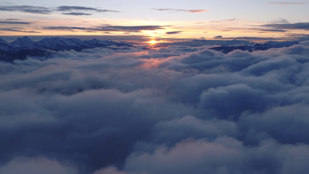 Sorvolando il mare di nuvole all'alba con una catena montuosa innevata in lontananza in Italia. Ripresa aerea.