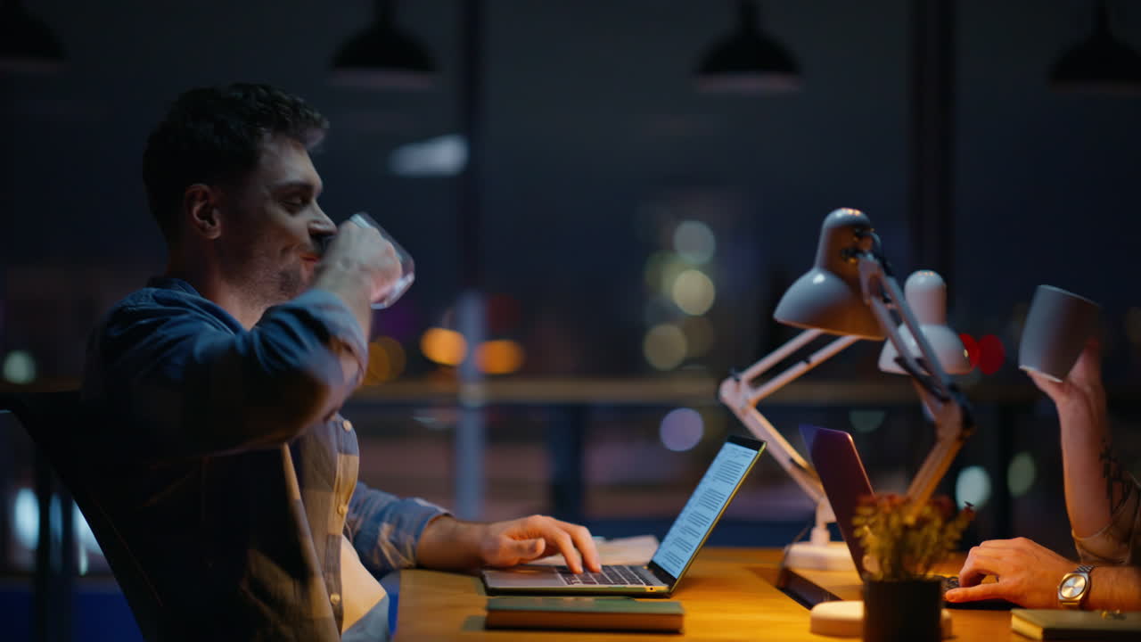 Late workers toasting coffee cups at evening cityscape room closeup. Men working
