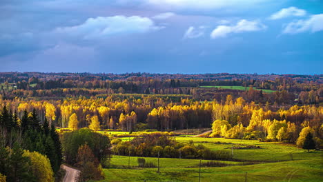 The-sun-and-white-clouds-glide-over-a-forest-landscape-with-green-meadows-in-between