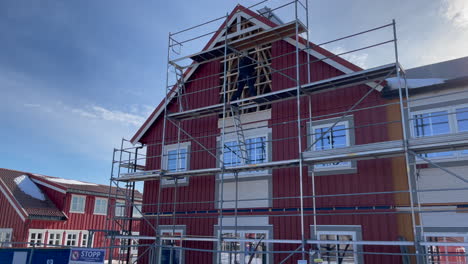 Hombre-Trabajando-En-Una-Casa-Tradicional-Noruega,-Parado-En-Un-Andamio-Arreglando-La-Pared-Principal