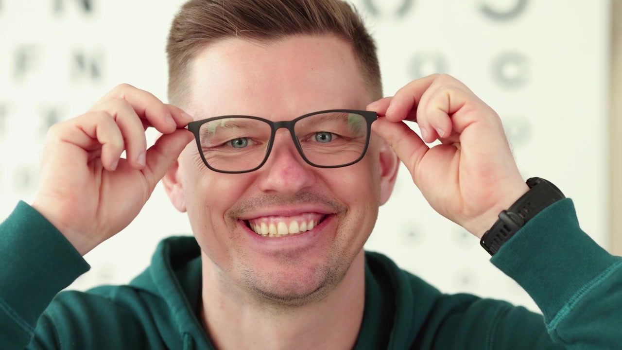 Positive man takes off glasses standing against snellen chart