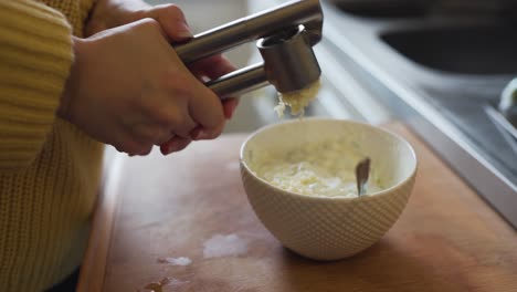 presionando un poco de ajo fresco en un tazón de pepino rallado y yogur griego