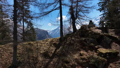 aerial reveal shot of snow covered mountains beyond a crest and through leafless trees blue sky and puffy clouds