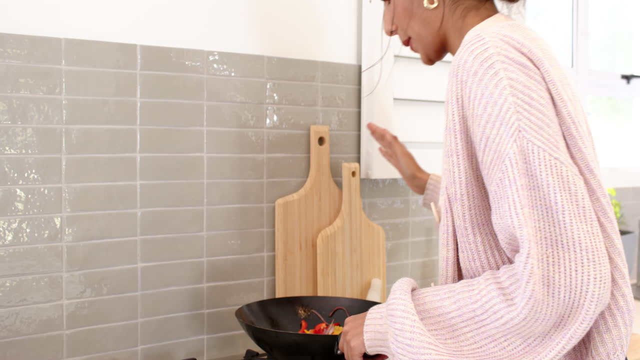 Femme indienne cuisinant des légumes dans un wok sur la cuisinière dans sa cuisine à la maison