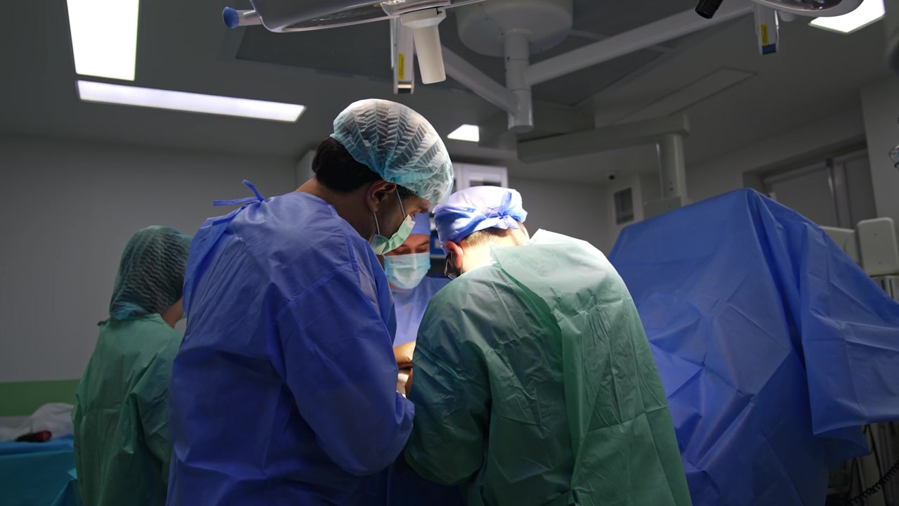Samarbejdende mandlige kirurger arbejder med traumeoperation. Lægerne står med ryggen til kameraet og bruger instrumenter under operationen.
