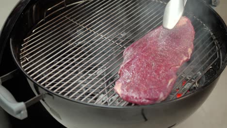 A-beef-steak-is-added-to-a-hot-charcoal-grill