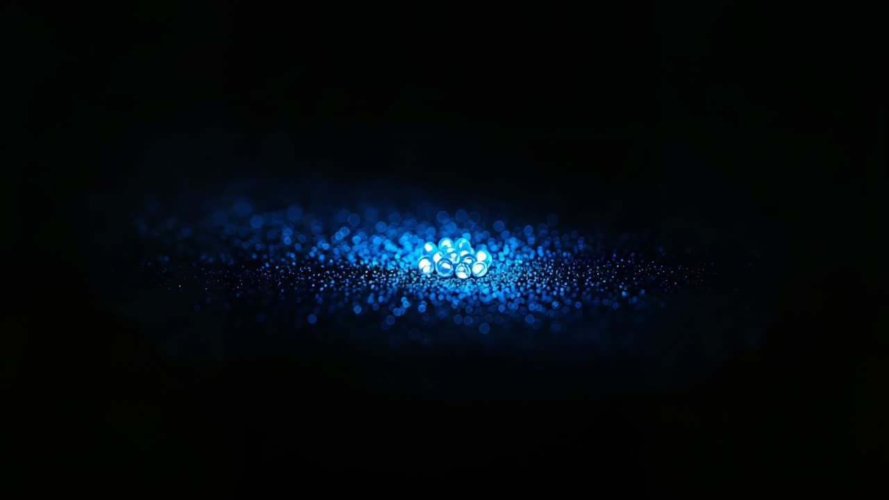 Pulsing cluster of blue beads responding to play starting on dark studio table, with shiny granules