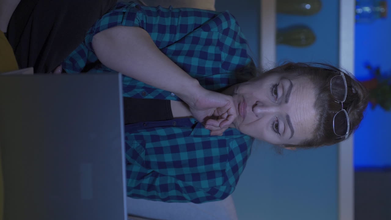 вертикальное видео женщины, глядящей на ноутбук с удивлением ночью дома.