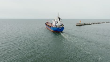 aerial establishing view of large blue cargo ship leaving port of liepaja , karosta bridge, slight overcast day, calm baltic sea, wide drone shot moving forward