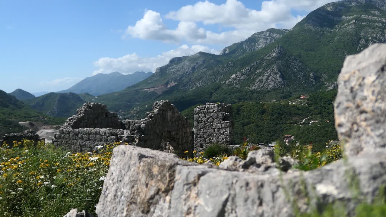 ruinas de una antigua fortaleza rodeada de muros de piedra y flores por las montañas