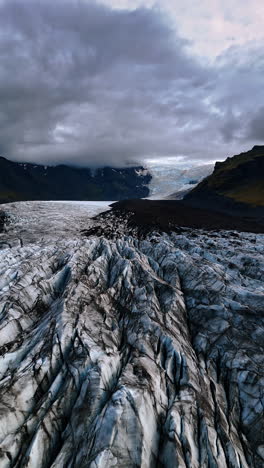 black and white glacier located among the mountains. dramatic cloudscape hanging over the rocky landscape of iceland. vertical video.