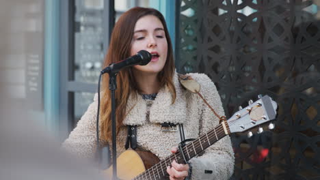 female musician busking playing acoustic guitar and singing to crowd outdoors in street