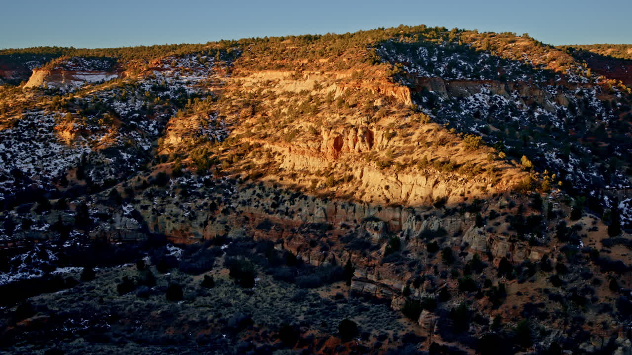 Sweeping drone shot of a dramatic red rock arch glowing in the golden sunrise.