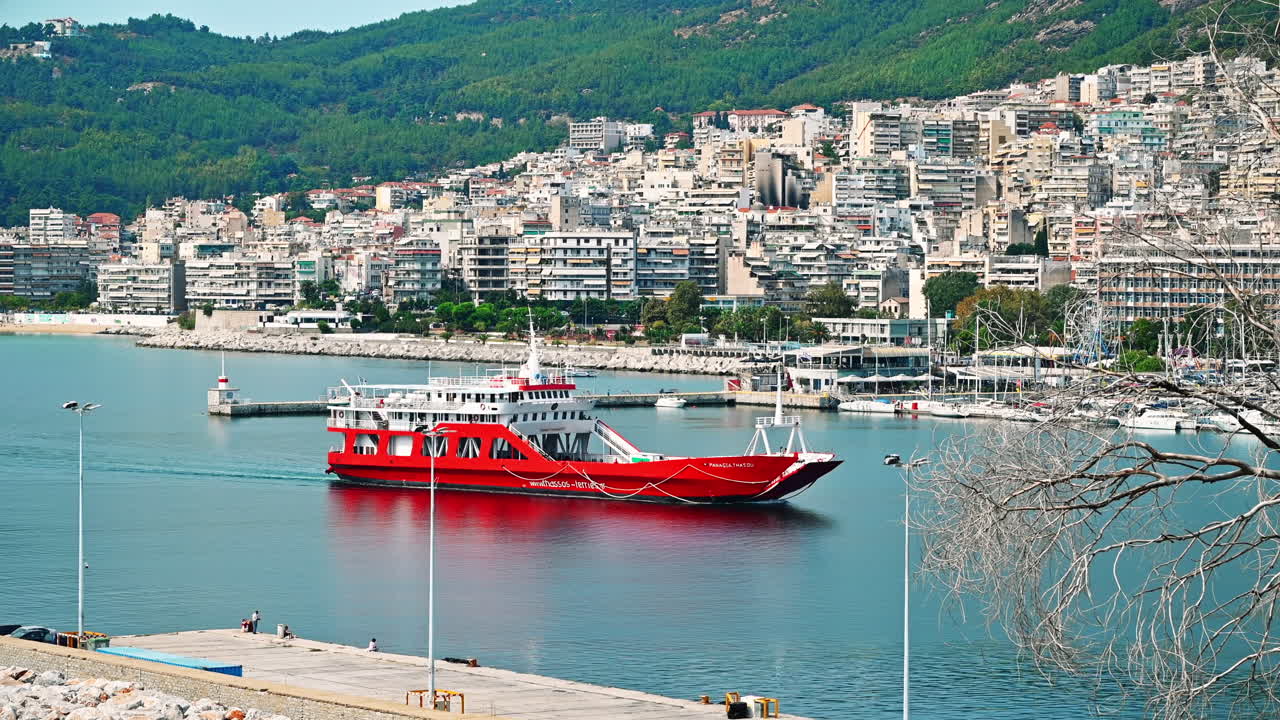 KAVALA, GREECE - SEPTEMBER 23, 2020: Moving red ship near the Aegean sea coast, multiple buildings on the background