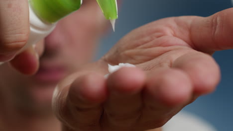 young man squeezing a white moisturizer from a tube on his hand close-up. morning routine. beauty and care concept.