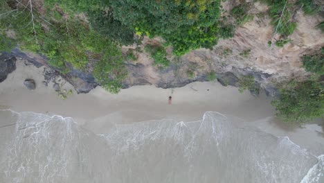 Luftaufnahme-Eines-Mädchens,-Das-Zwischen-Einer-Klippe-Und-Wellen-Des-Ozeans-Liegt,-Die-Zu-Ihren-Füßen-Krachen