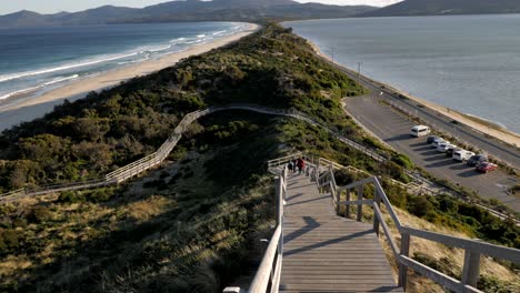 cacerola lenta hacia arriba sobre el cuello istmo paseo marítimo de madera en la isla bruny tasmania australia durante la ventosa tarde de primavera con olas rodando en la montaña del bosque de la costa de fondo