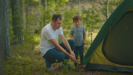 the boy helps his father to set up and assemble a tent in the forest. teaching children and travelling together in a tent camp