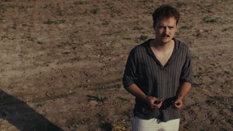 a man stands in a sparse field, looking down at his hands