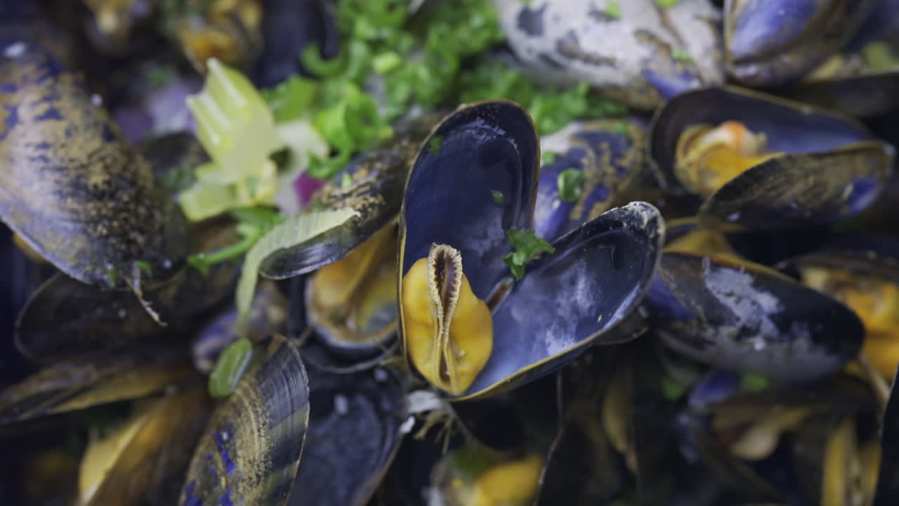 Close up of multiple steamy mussels in a pot with green onions on top