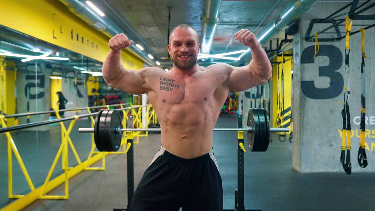 Uomo bodybuilder muscoloso che flette i muscoli e sorride in palestra