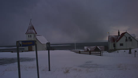 traditional icelandic church surrounded by snow, under dramatic arctic skies grey with storm near ocean