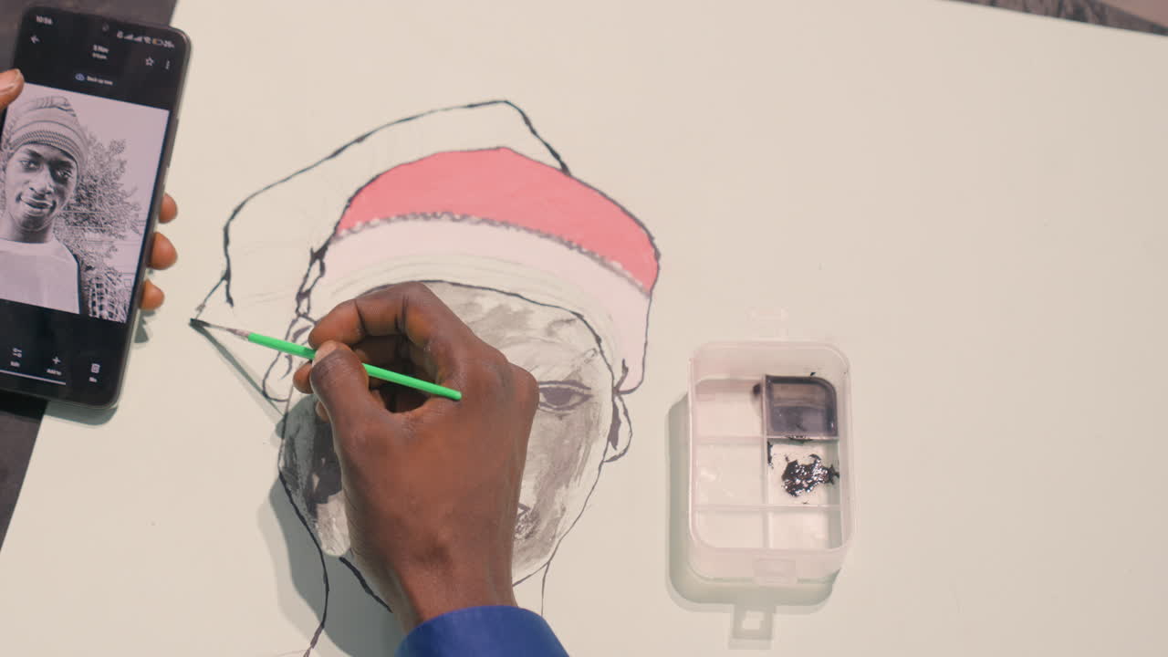 Artista afroamericano che inchiostra ritratti, con riferimento da telefono, mano ferma che delinea i contorni, pennello verde che inchiostra il bordo del cappello e la guancia, vista dall'alto dello studio, area di lavoro su carta bianca, tratti metodici e concentrato