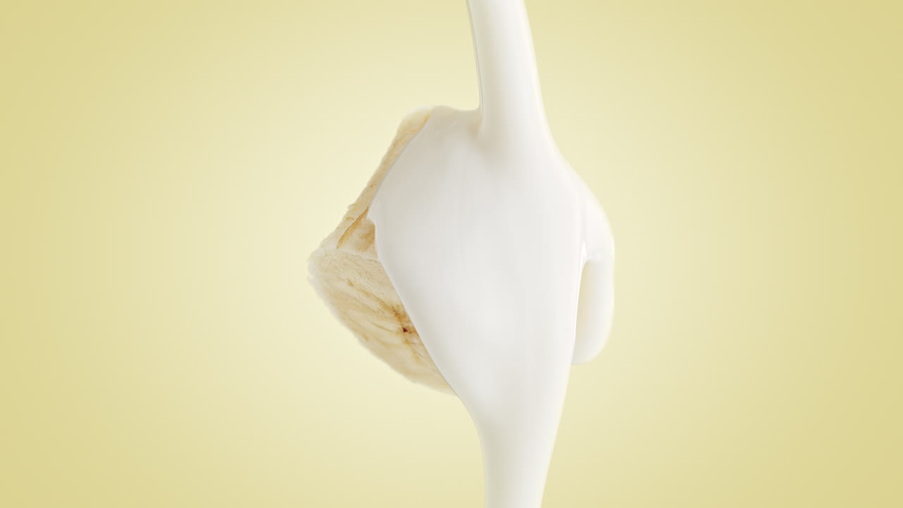 Yogurt cremoso che ricopre una banana morbida a fette su sfondo giallo in macro slow motion