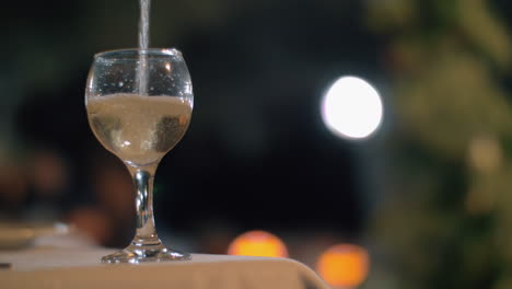 pouring white wine in outdoor restaurant at night