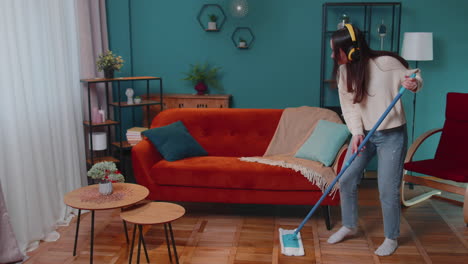 housekeeper young woman is mopping floor in apartment living room dancing listening to music at home