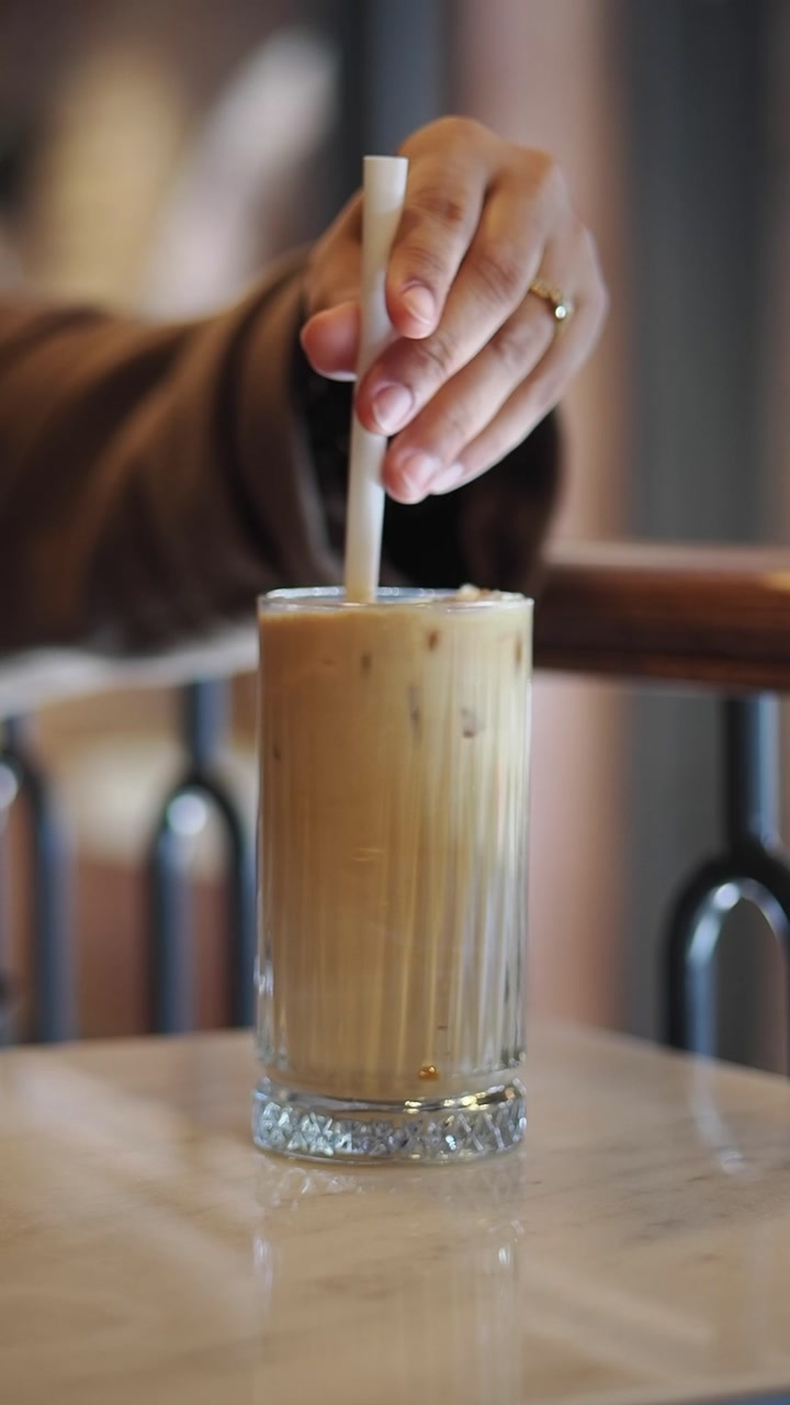 Close-up of Hand Stirring Iced Coffee with a Straw