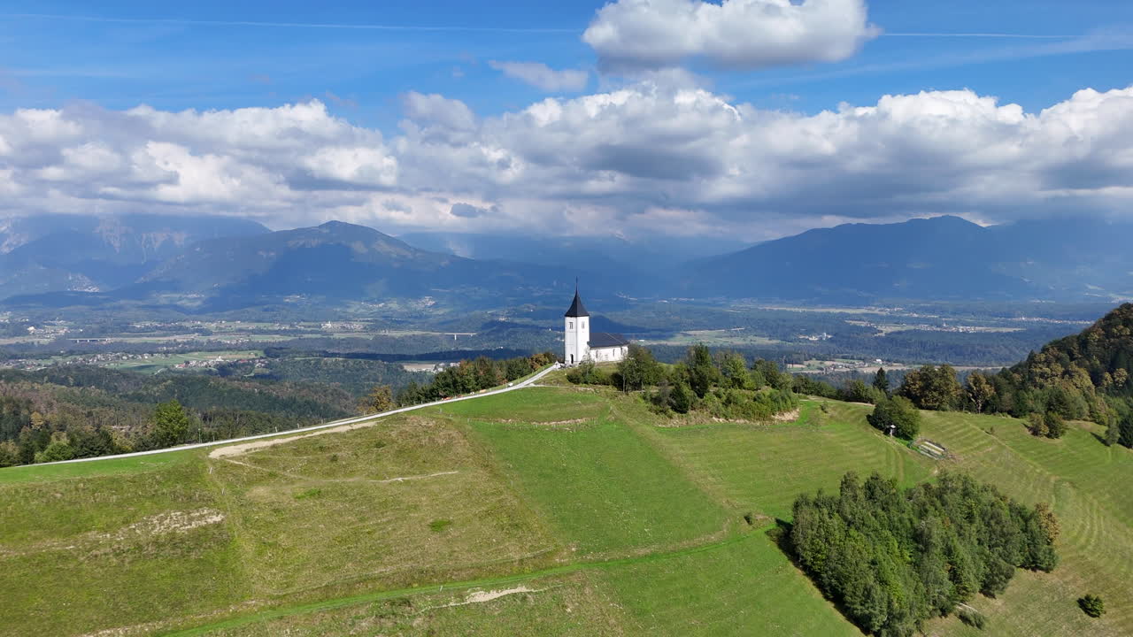 Pullback aerial view of historic catholic Church of Saint Primus at the top of a hill overlooking village of Jamnik Slovenia