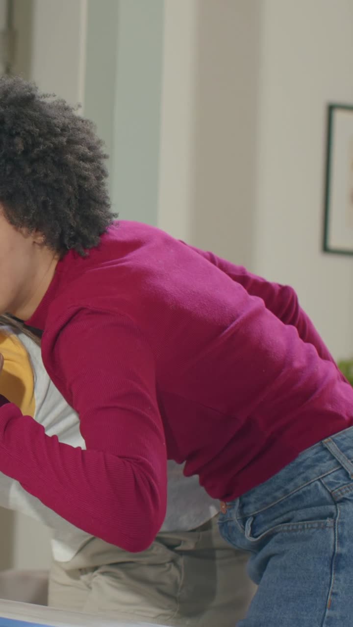 Vertical video: Rising from hug, woman in magenta top at home, calling hi and waving with watch