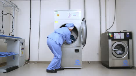 female worker take away clothes from drying machine at laundry room