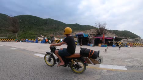 Tracking-shot-of-male-person-with-flip-flops-driving-on-motorbike-along-coastline-of-Vietnam