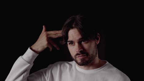 trendy young man pointing finger gun at head, close, black background