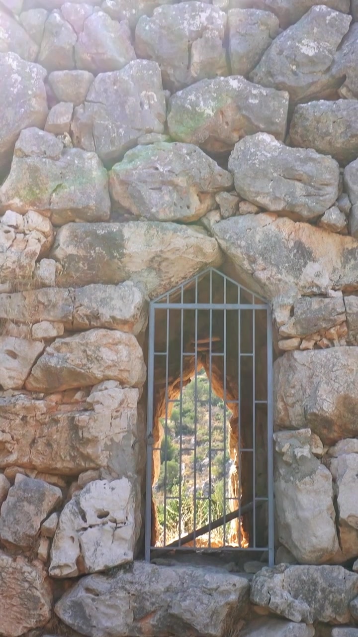 Finestra in muro di pietra con sbarre di ferro che rivela il paesaggio a Micene