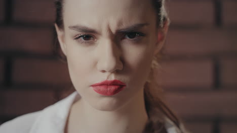 Beautiful-woman-frowning-face-and-looking-into-camera-on-brick-wall-background