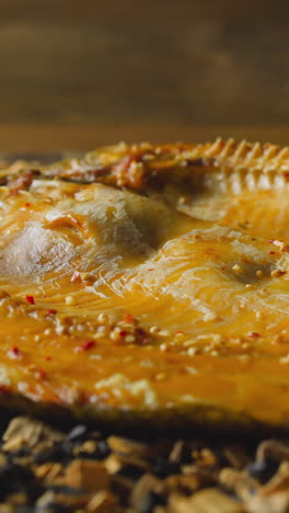 tasty dressed ide fish with spicy seasonings and crust lies on pile of decayed wooden chips and charcoals in smokehouse close view slow motion