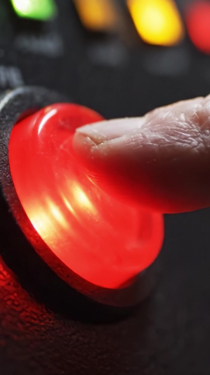 Vista Ravvicinata di un Pulsante Rosso Luminoso su un Pannello di Controllo, che evidenzia la superficie testurizzata e le luci circostanti in azione, evocando sensazioni di urgenza e attenzione.