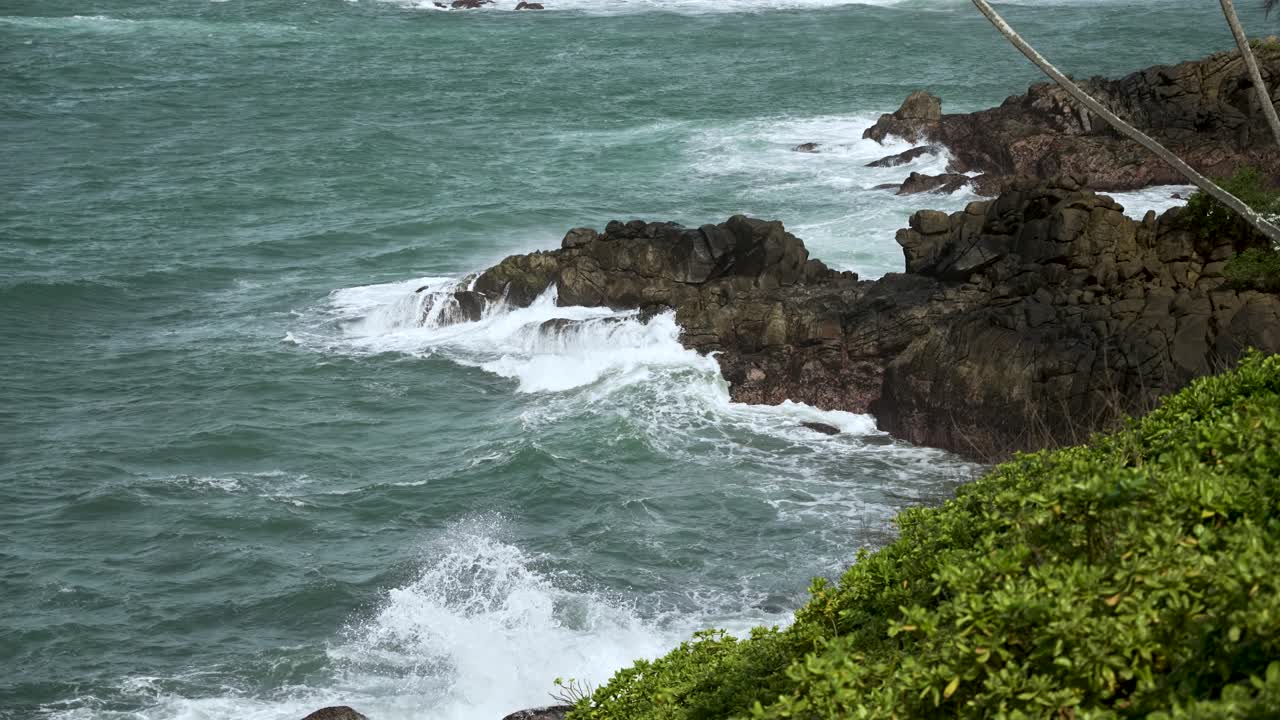 las olas blancas del océano se estrellan poderosamente sobre las rocas oscuras en el océano índico, creando espuma y pulverización contra un telón de fondo de cielos nublados.