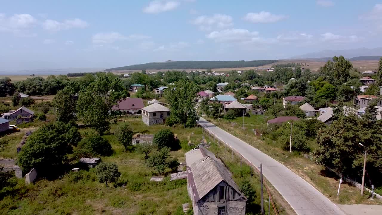 A serene village in the countryside, showcasing simple houses, green fields, and a calm road. The sky is bright and clear, ideal for exploring nature's beauty
